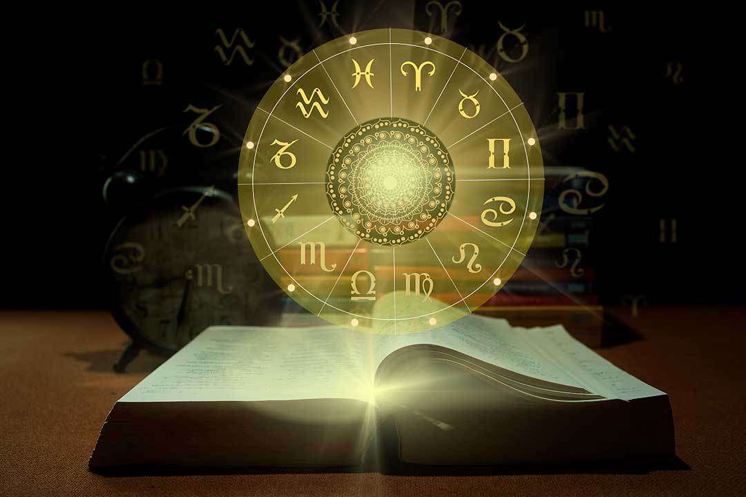 Um livro aberto pela metade. Saindo de suas páginas, como em holograma, o zodíaco com os signos. Previsões para os Signos em Maio