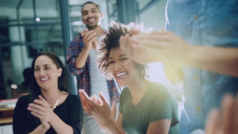 Filantropia: Foto de uma equipe de empresários criativos aplaudindo uma conquista enquanto trabalhava até tarde na sala de reuniões